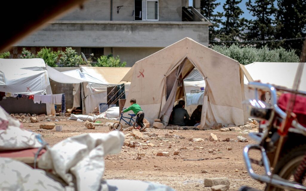 boy on bike outside tent in settlement camp